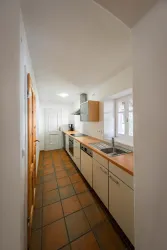 Eine moderne Küche mit Holzarbeitsplatten und hellen Schränken. Der Raum ist schmal und gut beleuchtet, mit einem Fliesenboden.