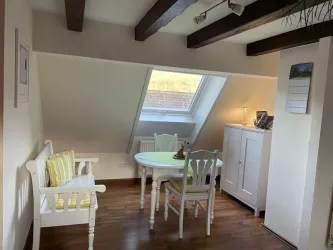 Ein gemütlicher Raum mit einem kleinen Tisch und zwei Stühlen. Die Dachfenster sorgen für viel Tageslicht und eine angenehme Atmosphäre.