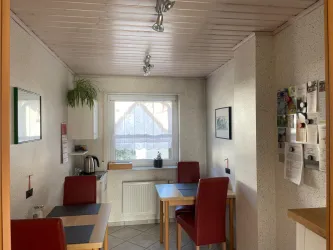 Eine kleine Küche mit einem Tisch und roten Stühlen. Das Fenster bietet Blick nach draußen, und es gibt eine Küchenzeile mit einem Wasserkocher.