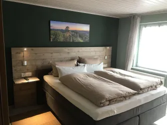 Ein modernes Schlafzimmer mit einem großen Bett und einer hübschen Wanddekoration. Es gibt viel Tageslicht und eine gemütliche Atmosphäre.