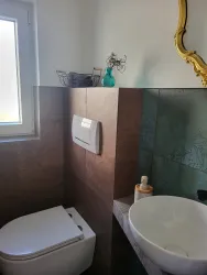 Ein modernes Badezimmer mit einer Toilette und einem Waschbecken. Es gibt eine große Fensteröffnung und dekorative Elemente.
