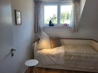 Ein gemütliches Zimmer mit einem Einzelbett und einem kleinen Tisch. Durch die Fenster scheint das Tageslicht und es gibt eine schöne Aussicht ins Grüne.