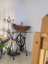 Ein dekorativer Tisch aus Metall mit einer Glasplatte steht in der Ecke. Daneben befinden sich eine Kerzenhalter, ein geflochtener Korb und frische Blumen.