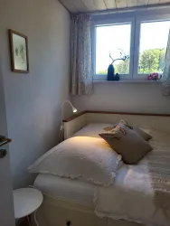 Ein gemütliches Schlafzimmer mit einem Einzelbett und zwei Kissen. Durch das Fenster strömt natürliches Licht und es gibt eine kleine Dekoration auf der Fensterbank.