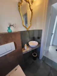 Ein modernes Badezimmer mit einem eleganten Waschbecken und einem großen Spiegel. Die Wandgestaltung kombiniert verschiedene Materialien und Farben.