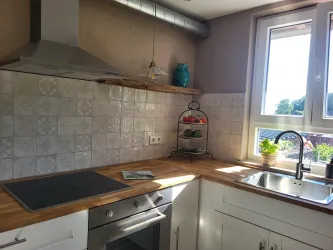 Eine moderne Küche mit einer Holzarbeitsplatte und weißen Schränken. Durch das Fenster strömt viel Tageslicht hinein.
