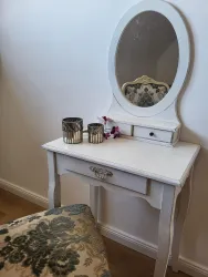 Ein eleganter Schminktisch mit einem runden Spiegel. Auf der Tischplatte stehen zwei Kerzenhalter und eine kleine Blume.
