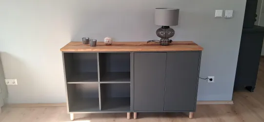 Ein modernes Sideboard aus Holz mit grauen Elementen steht an einer hellen Wand. Auf dem Sideboard befindet sich eine stilvolle Lampe und einige dekorative Gegenstände.
