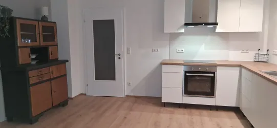 Eine moderne Küche mit weißen Möbeln und Holzoberflächen. Im Hintergrund steht ein elegantes schwarzes Sideboard.