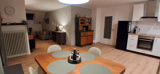 Eine moderne und einladende Küche mit einem Esstisch und Stühlen. Der Raum ist hell und gut eingerichtet, mit einem gemütlichen Wohnzimmerbereich im Hintergrund.