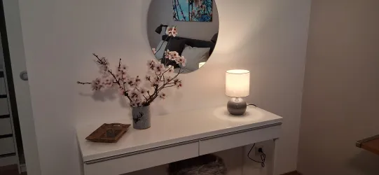 Ein eleganter Tisch mit einer runden Spiegel und einer Tischlampe. Vasen mit Blumenzweigen verleihen dem Raum eine frische Note.