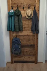 Ein rustikaler Flur mit einer Holzverkleidung. An der Wand hängen zwei Jacken, ein Hut und ein Rucksack.
