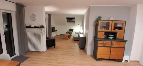 Ein modernes, helles Wohnzimmer mit Holzboden und eleganter Einrichtung. Die Möbel sind klar und zeitgemäß, mit einem kleinen Essbereich in der Nähe.