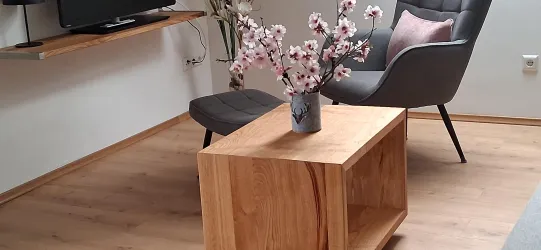 Ein gemütlicher Wohnraum mit einem Holzkaffee Tisch und einem Sessel. Auf dem Tisch steht eine Vase mit blühenden Zweigen.