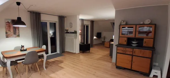 Ein helles und modernes Wohnzimmer mit einem Essbereich. Die Möbel sind minimalistischer und funktionaler Stil, mit großen Fenstern für viel Tageslicht.