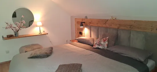 Ein gemütliches Schlafzimmer mit einem großen Bett und einer warmen Beleuchtung. An der Wand befindet sich ein runder Spiegel und eine Holzablage.