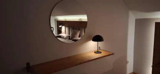 Ein modernes Zimmer mit einem runden Spiegel und einer stilvollen Lampe auf einem Holzregal. Der Platz strahlt Gemütlichkeit und Eleganz aus.