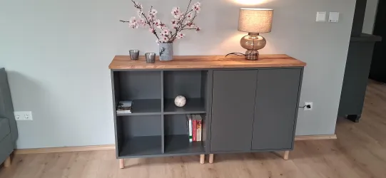 Ein modernes Sideboard in einem Wohnzimmer mit einem Holztisch und einer Lampe. Auf dem Tisch stehen Blumen und einige dekorative Gegenstände.