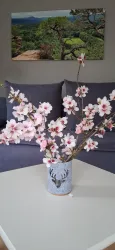 Eine Vase mit blühenden Kirschblüten steht auf einem Tisch. Im Hintergrund ist ein Landschaftsbild zu sehen.