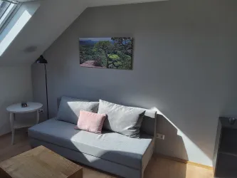 Ein gemütliches Wohnzimmer mit einem grauen Sofa und einem kleinen Tisch. An der Wand hängt ein Bild von einer Landschaft.