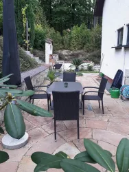 Ein schöner Außensitzbereich mit einem Tisch und Stühlen aus Rattan. Umgeben von Pflanzen und dem beruhigenden Grün der Natur.