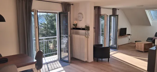 Eine moderne Wohnung mit großen Fenstern und einem Balkon. Der Raum ist hell und einladend mit minimalistischem Mobiliar.