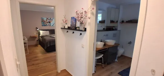 Ein einladender Flur mit einem Schlafzimmer auf der linken Seite und einem modernen Badezimmer auf der rechten Seite. Die Wände sind hell, und der Boden ist aus Holz.