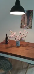 Ein gemütlicher Esstisch mit einem Glas Wein und einer Vase voller Kirschblüten. An der Wand hängt ein Bild einer malerischen Tür.