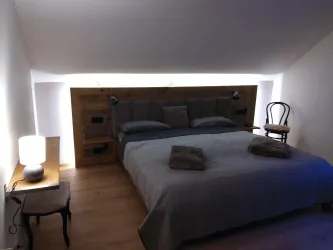 Ein modernes Schlafzimmer mit einem großen Bett und sanfter Beleuchtung. Neben dem Bett steht ein Tisch mit einer Lampe und einem Stuhl.
