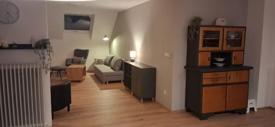 Ein modern eingerichteter Wohnbereich mit einem gemütlichen Sofa und einem Holzschrank. Die Wände sind in neutralen Farben gehalten, und es gibt ein Fenster, das für natürliches Licht sorgt.