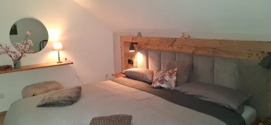 Ein gemütliches Schlafzimmer mit einem großen Bett und einem Holzkopfteilen. Sanftes Licht und dekorative Elemente verleihen dem Raum eine entspannte Atmosphäre.