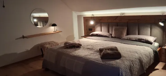 Ein modernes Schlafzimmer mit einem großen Bett und eleganter Beleuchtung. Die Wände sind in neutralen Farben gehalten und es gibt einen runden Spiegel.