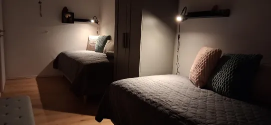 Ein einfaches Zimmer mit zwei Einzelbetten. Es ist schwach beleuchtet und hat eine ruhige Atmosphäre.