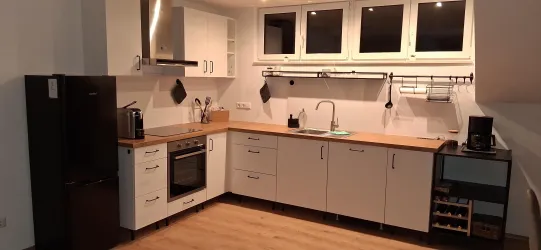 Eine moderne Küche mit weißen Schränken und Holzarbeitsflächen. Sie ist gut ausgestattet mit Geräten und Fenstern, die viel Licht hereinlassen.