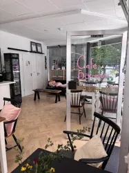 Ein gemütliches Café mit modernen Möbeln und einladenden Dekorationen. Die Fenster ermöglichen viel Tageslicht und eine angenehme Atmosphäre.