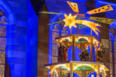 Eine hölzerne Weihnachtspyramide mit den Heiligen Drei Königen vor einer beleuchteten Kirche auf dem Weihnachtsmarkt in Neustadt.