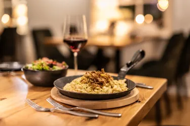 Auf einem Restauranttisch stehen Spätzle in einer Gusspfanne, ein Beilagensalat und ein Glas Rotwein.