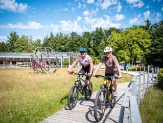 Zwei Personen befinden sich mit ihrem Mountainbike am Haus der Nachhaltigkeit in Johanniskreuz.