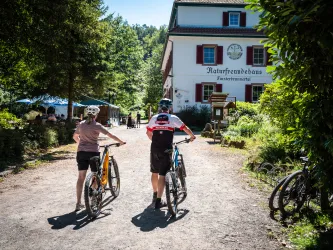 Zwei Personen schieben ihr Mountainbike in Richtung Naturfreundehaus Finsterbrunnertal für eine Rast.