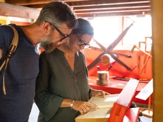 Zwei Personen sehen sich die Ausstellungsstücke im Museum Alte Samenklenge an während ein Gästeführer sie durch das Museum begleitet.