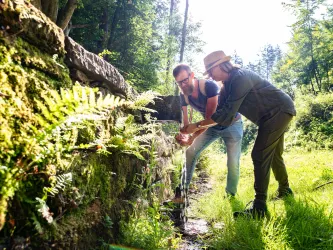 Zwei Personen erfrischen ich an dem fließenden Wasser des Straufelsbrunnen.