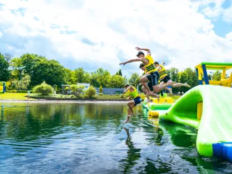Kinder springen von einem Wasserparkturm im Strandbad ins Wasser.