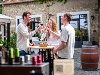 Menschen stehen in einem Weingutshof und genießen ein Glas Wein.