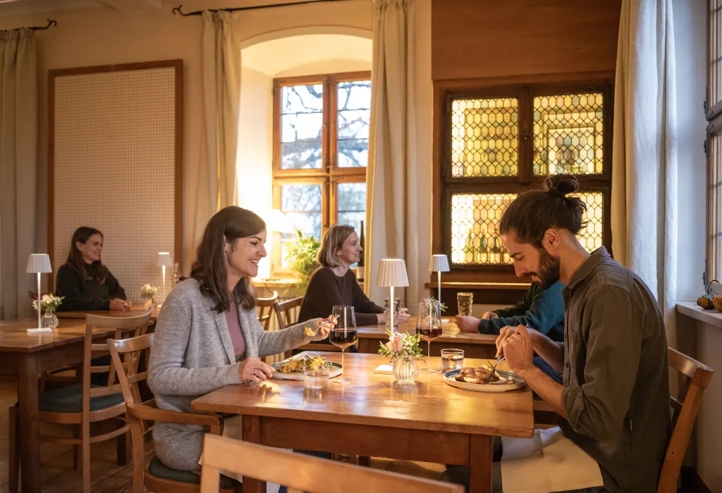 Mehrere Personen sitzen an Tischen in einem Restaurant und genießen ihre Gerichte und Wein.