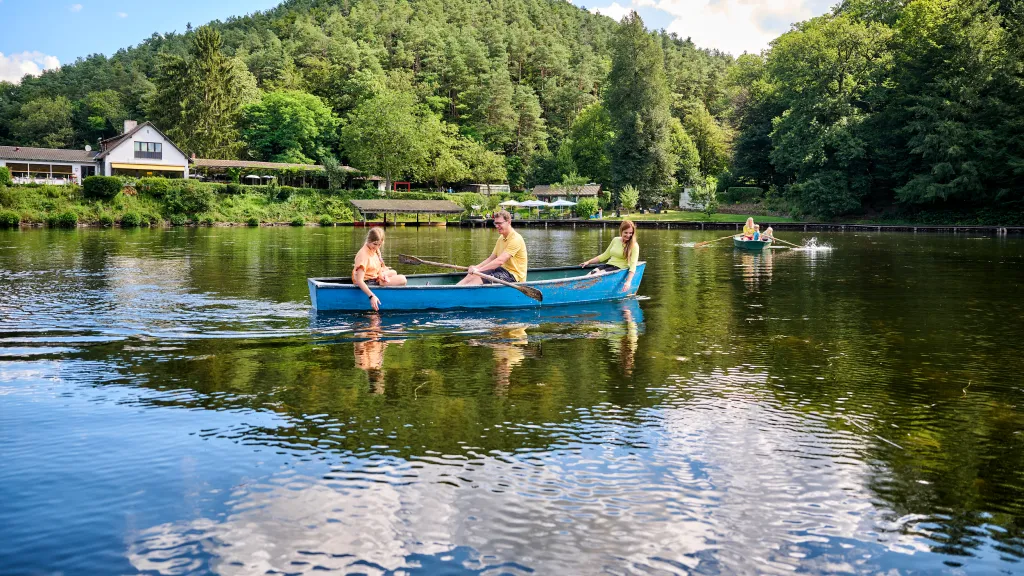 Eine Familie fährt mit einem Ruderboot über einen Weier.