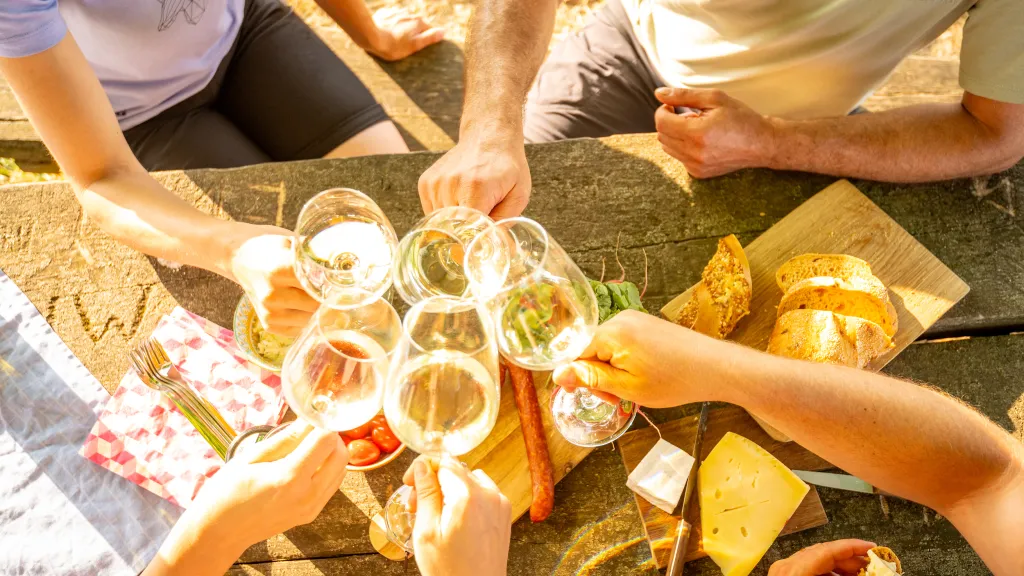 Menschen stoßen mit Weingläsern an einem Rastplatztisch mit Snacks an.