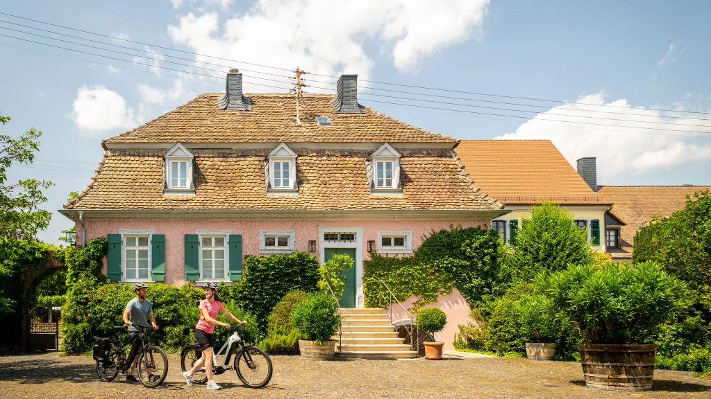 Eine schöne alte Villa mit rosa Fassade. Zwei Personen auf dem Rad stehen davor.
