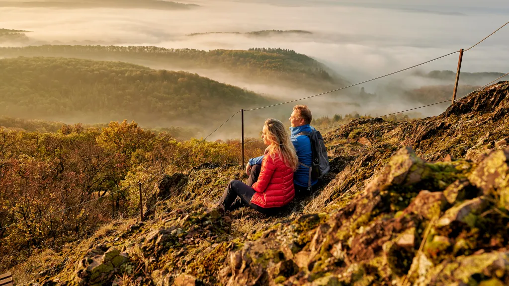 Zwei Personen betrachten den Ausblick über die Wälder und Hügel am Donnersberg.