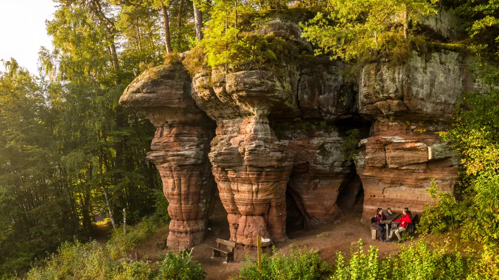 Wanderinnen und Wanderer sitzen vor einem Sandsteinfelsen am Rodalber Felsenwanderweg.