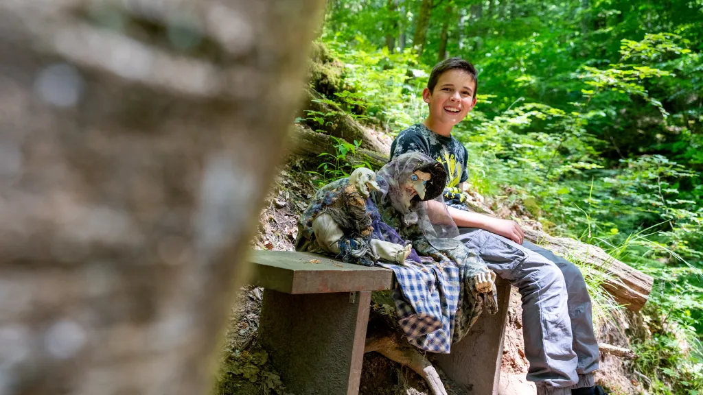 Wanderung mit Kids in der Hexenklamm bei Pirmasens (© CC-BY Pfalz Touristik, Fachenbach Medien) Ein Kind sitzt auf einer Bank auf der eine Hexenfigur platziert ist.